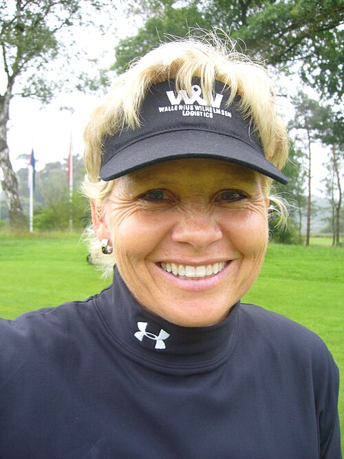 Smiling portrait of South African professional golfer Laurette Maritz in a visor and dark top, outdoors on a golf course.